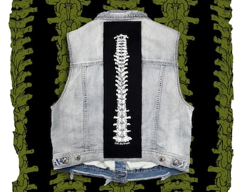 May include: A light blue denim vest featuring a long, rectangular black patch centered on the back. The patch displays a white, detailed illustration of a human spine with the text "Cuty Dog Design" printed in white at the bottom of the patch.