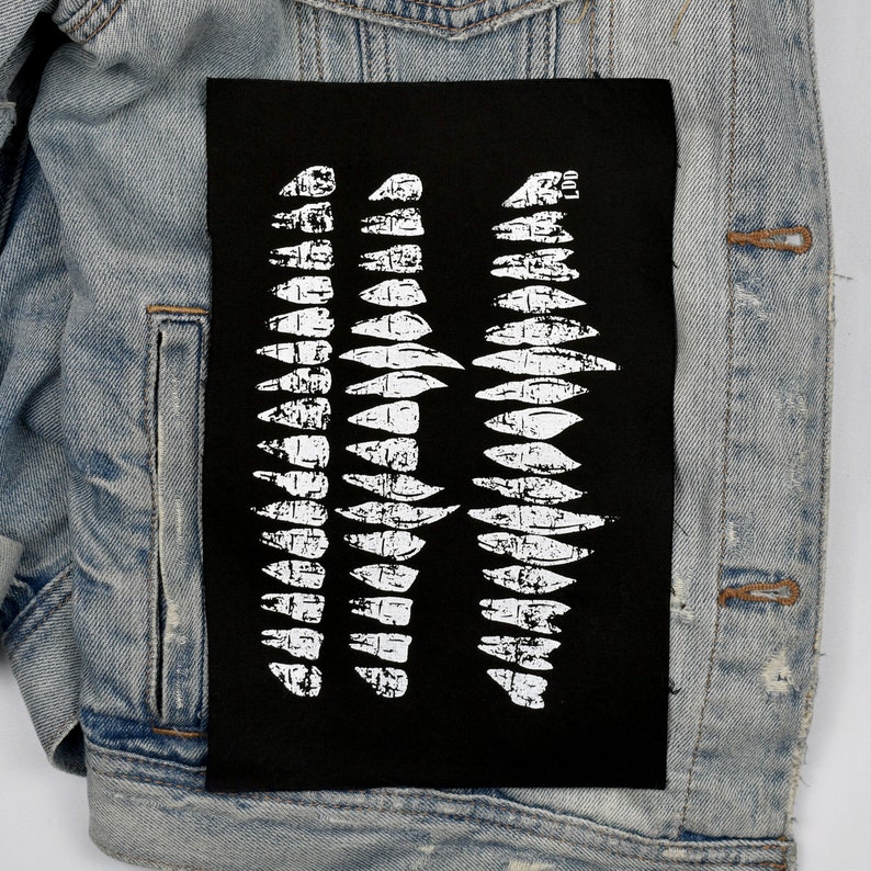 May include: Black fabric patch with a white graphic design of three rows of jagged, tooth-like shapes.