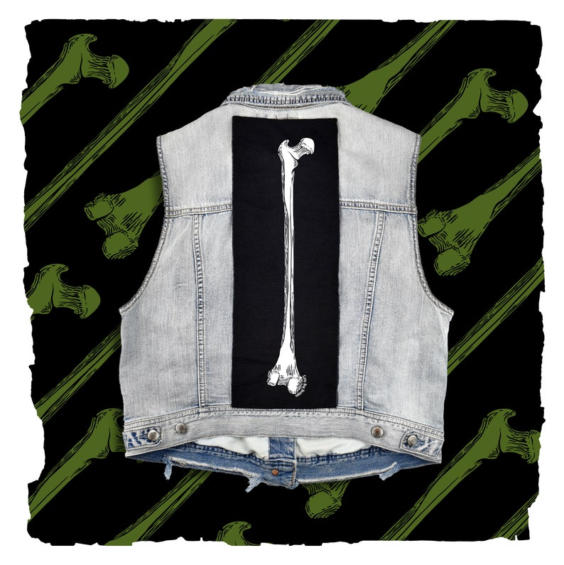 Op de afbeelding: Een denim vest met een zwarte patch met een witte omtrek van een lang bot. Het vest is tegen een achtergrond van diagonale groene botten op een zwarte achtergrond.