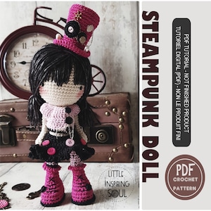 Peut inclure: Une poupée en crochet avec des cheveux noirs, un chapeau steampunk rose et noir, une robe rose et noire et des bottes roses. La poupée est debout sur une surface en bois avec une horloge et une valise en arrière-plan. Le texte "STEAMPUNK DOLL" est écrit en lettres blanches sur fond noir.