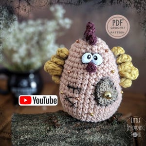 Peut inclure: Un poulet au crochet fait à la main avec de grands yeux globuleux, une crête violette et des plumes latérales jaunes. Le poulet est rose clair avec des accents dorés et des détails cousus en noir. Le texte "PDF Crochet Pattern" est inclus.