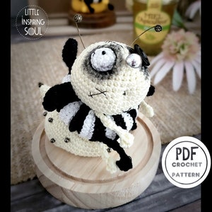 Peut inclure: Un modèle de crochet pour un jouet amigurumi abeille nommé "Buzzy the Bee". Le modèle est disponible en téléchargement PDF. L'abeille est blanche et noire avec un chapeau noir et une antenne en fil de fer.