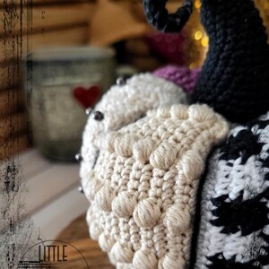 May include: A crocheted amigurumi toy with a white, black and purple body. The toy has a large, curled black horn and a textured white body.