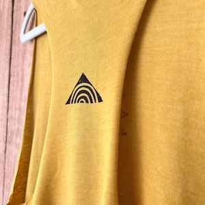 K&ouml;nnte beinhalten: Ein senfgelbes &auml;rmelloses Shirt mit einem schwarzen Dreiecksdesign, das einen Regenbogen im Inneren zeigt.