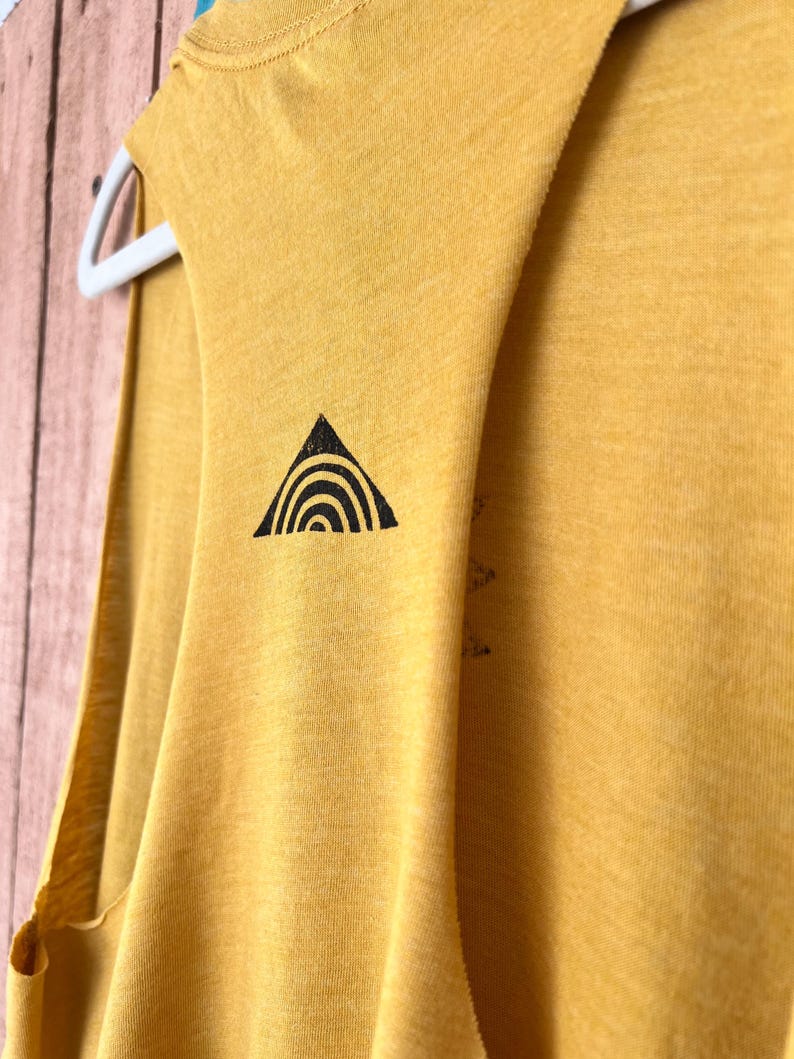 K&ouml;nnte beinhalten: Ein senfgelbes &auml;rmelloses Shirt mit einem schwarzen Dreiecksdesign, das einen Regenbogen im Inneren zeigt.
