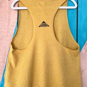 K&ouml;nnte beinhalten: Ein &auml;rmelloses Crop-Top in Senfgelb mit einem schwarzen Dreiecksdesign auf der R&uuml;ckseite. Das Dreieck hat eine geschwungene Linie im Inneren.