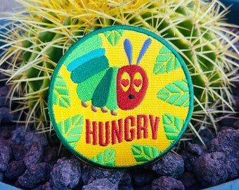 May include: A yellow, green, and red embroidered patch with a caterpillar and the word "HUNGRY" on a cactus.
