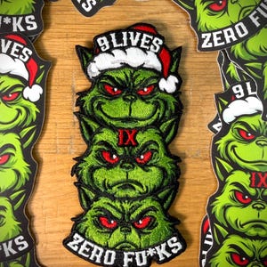 May include: Green embroidered patch featuring a stacked Grinch design wearing a Santa hat. The patch has the text "9 Lives" and "Zero F*cks". Additional patches with the same design are visible.