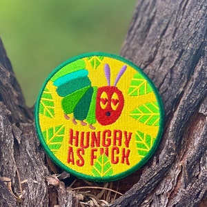 May include: A round yellow embroidered patch with a green caterpillar and the text "HUNGRY AS F*CK".
