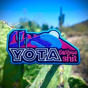 May include: A blue and pink embroidered patch with the text "YOTA Off Road Shit" and a desert landscape design.