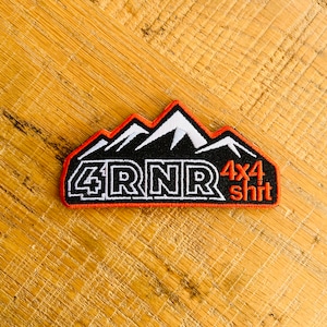 May include: A black and white embroidered patch with a mountain range design and the text "4RNR 4x4 shirt". The patch has a red border.