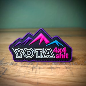 May include: Black patch with a white outline of the word "YOTA" and the words "4x4 shit" in pink. The patch features a stylized mountain range in purple, pink, and blue.