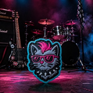 May include: A rubberized patch featuring a stylized gray cat head with a bright pink mohawk, pink-rimmed sunglasses, and a black spiked collar. The design is outlined in a vibrant cyan blue border, creating a bold and graphic aesthetic.