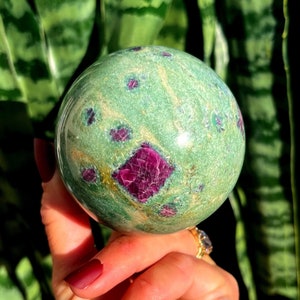 Pode incluir: Uma esfera verde e rosa com uma superfície lisa e polida. A esfera é feita de um tipo de gema com um padrão de redemoinho de verde, rosa e ouro.