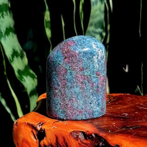 May include: A polished, cylindrical mineral specimen featuring a mottled texture with deep blue and vibrant magenta-pink colorations throughout. The stone has a smooth, rounded top and a flat base, displaying natural crystalline inclusions and variations.