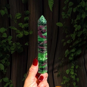 May include: A polished, hexagonal crystal tower featuring a vibrant mix of deep green zoisite and patches of magenta ruby. The stone has a pointed top and a smooth, multi-faceted surface with visible natural mineral inclusions throughout.