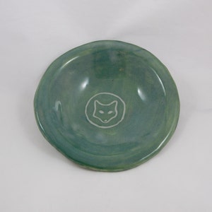 May include: A small, teal green ceramic bowl with a white fox silhouette in the center.