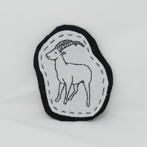 May include: Black and white embroidered patch of an antelope with curved horns on a white background with a black border.