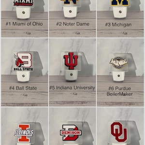 May include: A collection of nine night lights featuring college team logos. Each night light has a white base and a clear, rectangular top with a team logo and name. The logos include Miami RedHawks, Notre Dame, Michigan, Ball State, Indiana University, Purdue, Illinois, Denison, and Oklahoma.