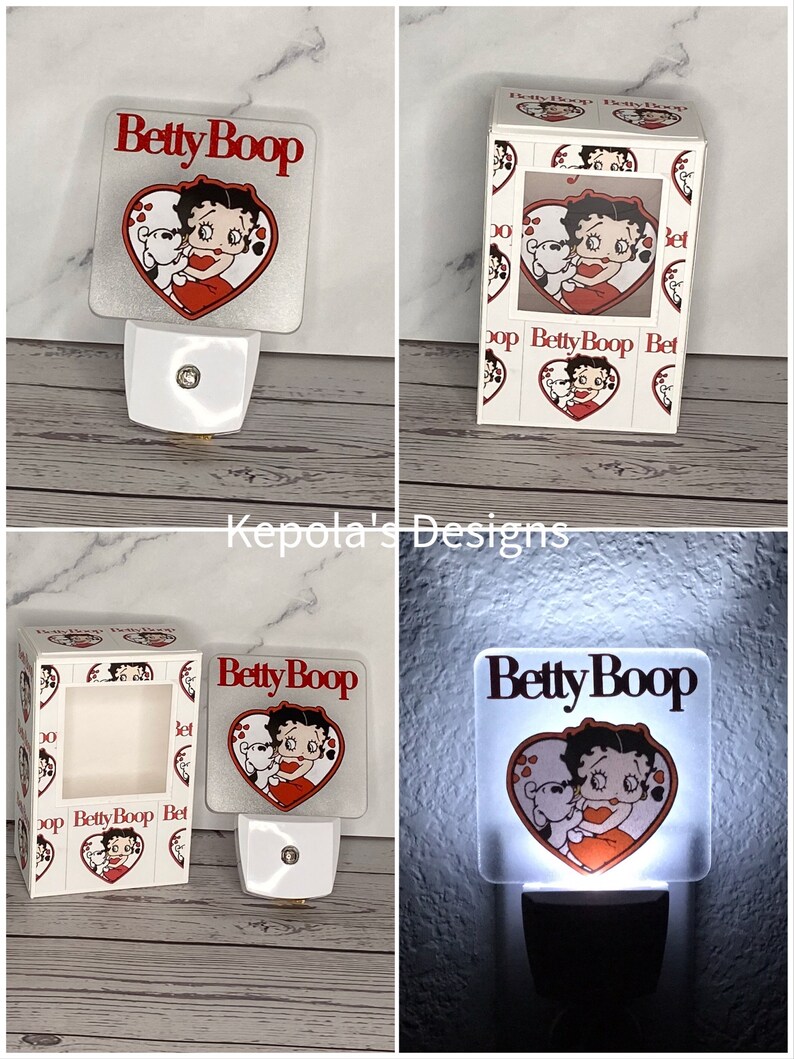 May include: A square, white night light featuring the cartoon character Betty Boop embracing a teddy bear inside a red heart. The words "Betty Boop" are above the heart in red. The night light is plugged into a white outlet.