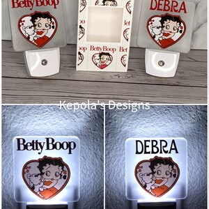 May include: White night lights featuring a Betty Boop design with a heart-shaped graphic. One night light is personalized with the name "Debra". The packaging box also features the Betty Boop design.