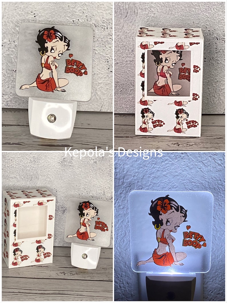 May include: A white night light featuring a square, translucent panel with a Betty Boop graphic. The cartoon character is depicted in a red outfit, with the words "Betty Boop" in red. The night light is plugged into a white base.