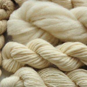 Puede incluir: Primer plano de varios ovillos de hilo en varios tonos de crema y beige. El hilo es suave y esponjoso, perfecto para tejer o hacer ganchillo.