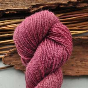 May include: A skein of deep pink yarn, twisted into a figure eight shape. The yarn is soft and fluffy, and it is perfect for knitting or crocheting.