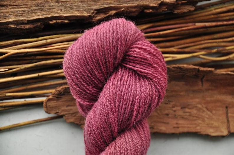 May include: A skein of deep pink yarn, twisted into a figure eight shape. The yarn is soft and fluffy, and it is perfect for knitting or crocheting.