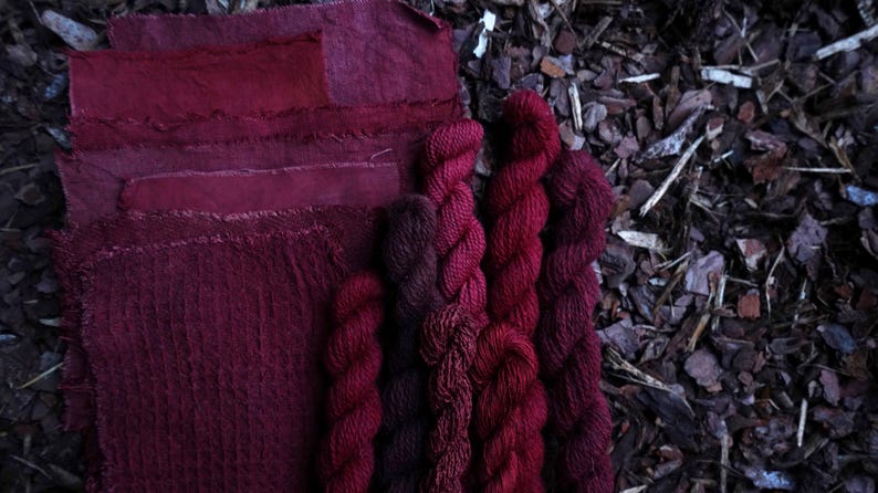 May include: A collection of hand-dyed yarn in shades of burgundy and dark red, displayed with fabric swatches in matching colors.