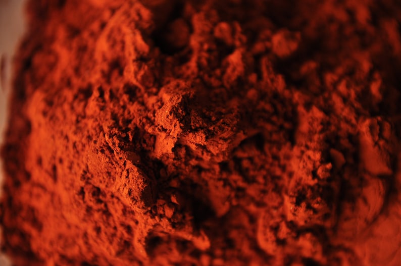 May include: Close-up of a pile of red powder. The powder has a fine, granular texture and a deep, rich color.