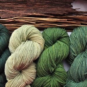 May include: Four skeins of yarn in shades of green and beige. The yarn is arranged in a figure of eight shape.