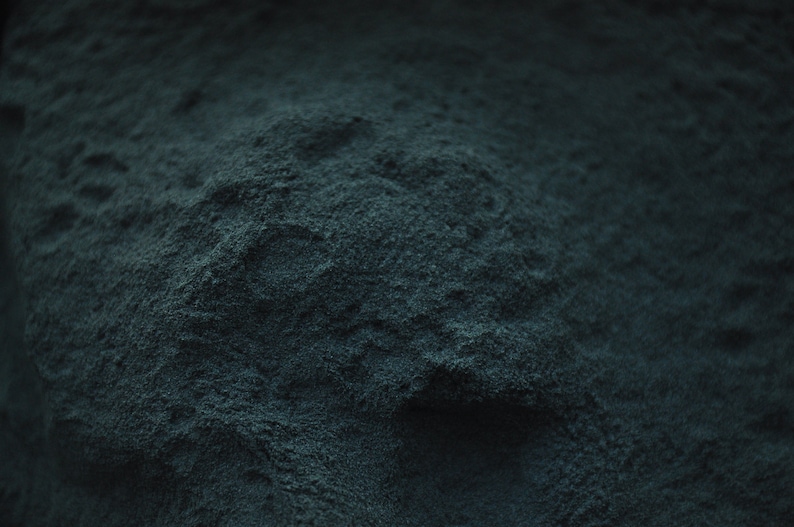 May include: Close-up of a dark blue powder, possibly spirulina or blue algae, with a textured surface.