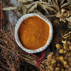 May include: A small white ceramic bowl filled with orange spice powder, surrounded by dried flowers and grasses.