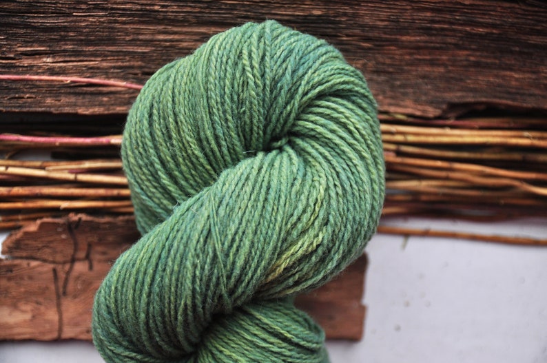 May include: A skein of green yarn with a subtle ombre effect, wound into a ball shape. The yarn is soft and textured, perfect for knitting or crocheting.