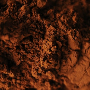 May include: Close-up of a pile of dark brown cocoa powder. The powder has a rough, textured surface.