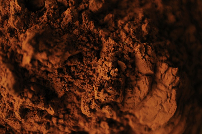 May include: Close-up of a pile of dark brown cocoa powder. The powder has a rough, textured surface.