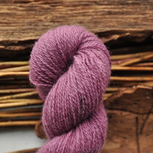 May include: A skein of soft, purple yarn, twisted into a loop. The yarn is made of natural fibers and has a rustic, hand-spun look.