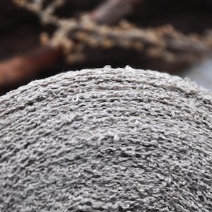 May include: Close-up of a grey, textured, circular object made of woven fibres. The object has a rough, uneven surface and appears to be made of natural materials.