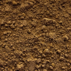 May include: Close-up of a brown, grainy powder. The powder has a rough texture and is made up of small, irregular particles.