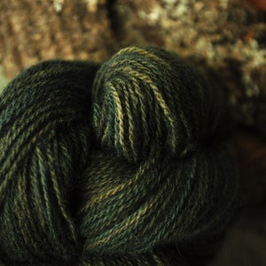 May include: Close-up of a skein of yarn in shades of green and brown. The yarn is twisted and knotted, creating a textured and organic look.