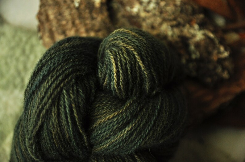 May include: Close-up of a skein of yarn in shades of green and brown. The yarn is twisted and knotted, creating a textured and organic look.
