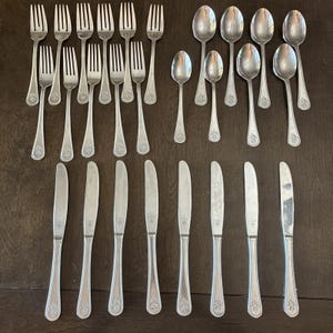 May include: A collection of twenty-two stainless steel flatware pieces, including eleven forks, seven spoons of varying sizes, and eight dinner knives. Each utensil features a polished finish and a decorative floral motif at the handle base.