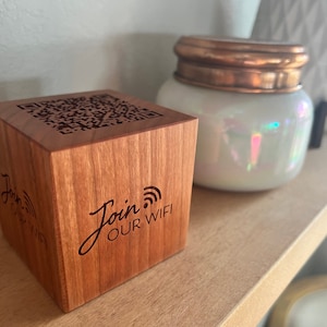May include: A small wooden cube with a QR code and the text "Join Our WiFi" engraved on it. The cube is sitting on a wooden surface.