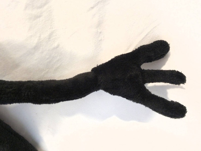 Puede incluir: Brazo de peluche negro con tres dedos extendidos, el brazo est&aacute; doblado en el codo.