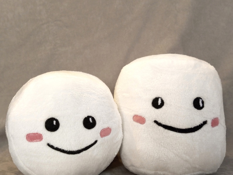 May include: Two white plush toys shaped like marshmallows with black eyes and a black smiling mouth. Each toy has pink blush on its cheeks.