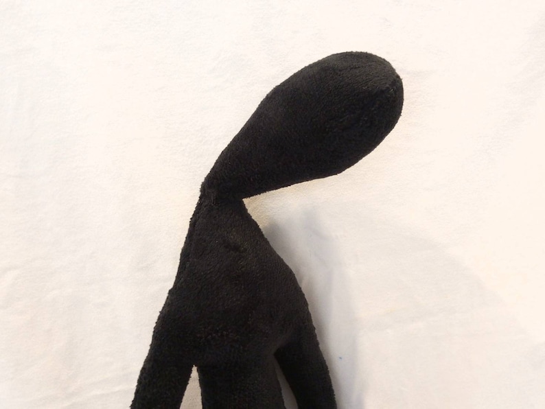 Puede incluir: Juguete de peluche negro con forma de persona, cuello largo y cabeza inclinada hacia abajo. El juguete est&aacute; hecho de tela suave y peluda.
