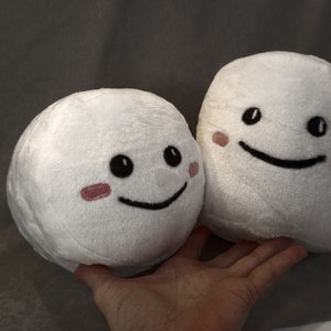 May include: Two white plush toys with smiling faces. Both toys have black eyes and mouths, and pink cheeks.