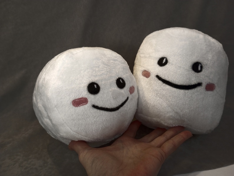May include: Two white plush toys with smiling faces. Both toys have black eyes and mouths, and pink cheeks.