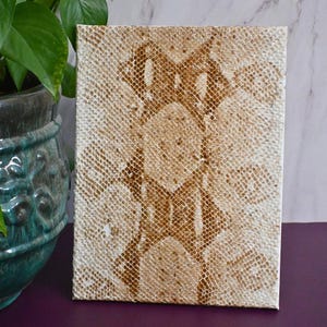 May include: A white canvas with a brown snakeskin pattern painted on it. The pattern is a repeating design of scales.